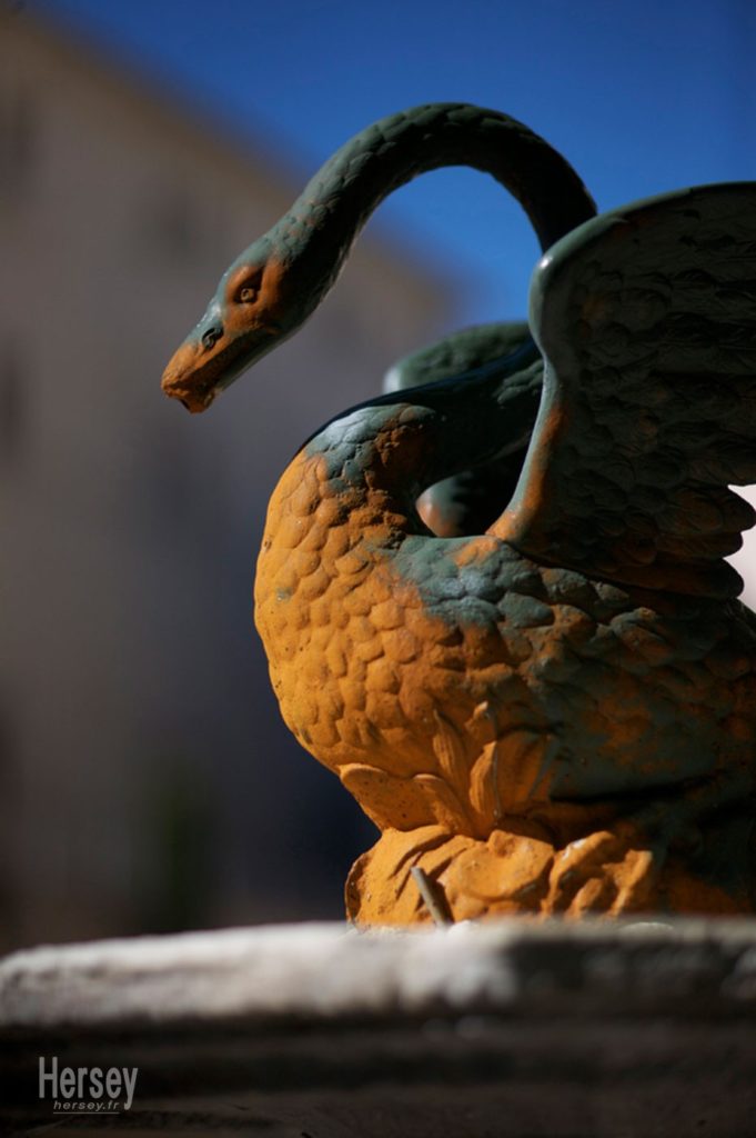 Fontaine au Cygne à Uzès Gard Occitanie - représentation en sculpture de métal d'un animal faisant penser à un cygne - la sculpture est à moitié rouillée - couleur ocre © Hersey Photographe Uzès